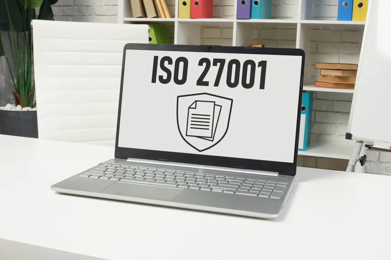 ISO 27001 documentation and laptop on a desk