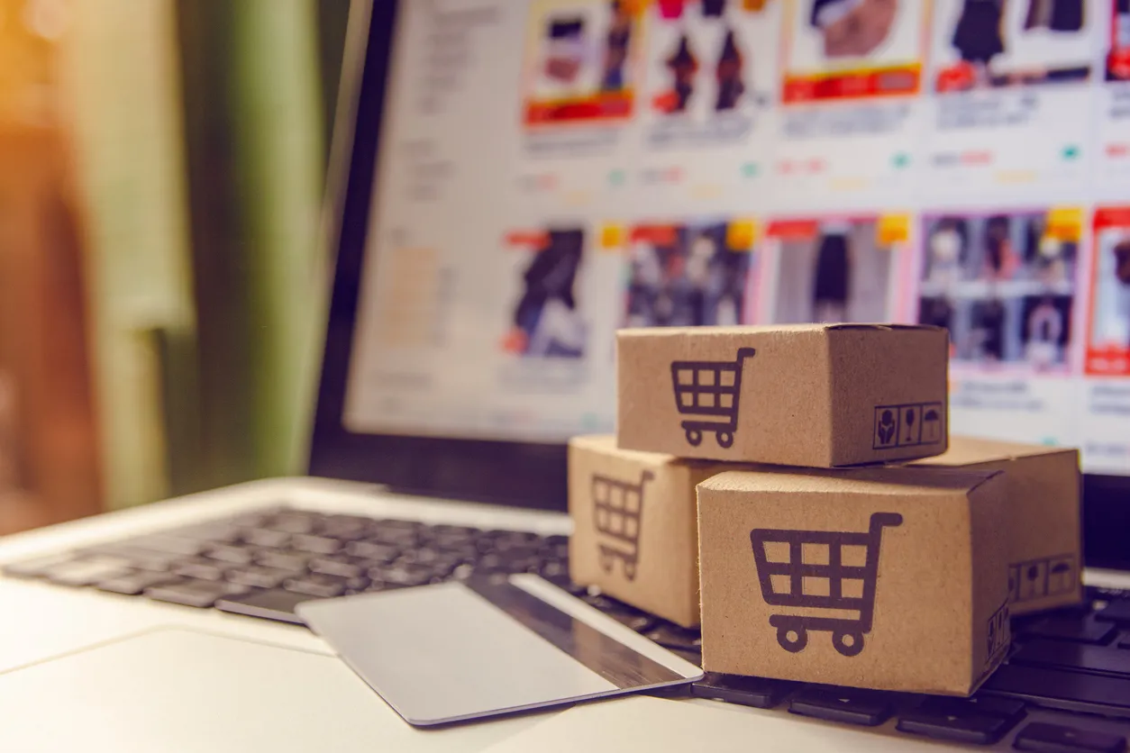 Laptop showing an online store product page beside a card reader and packaged parcels on a desk.