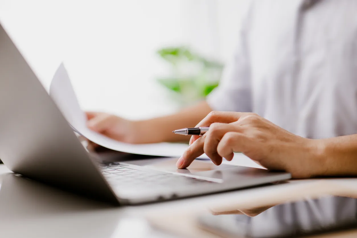 Two compliance documents side by side on an office desk with a laptop