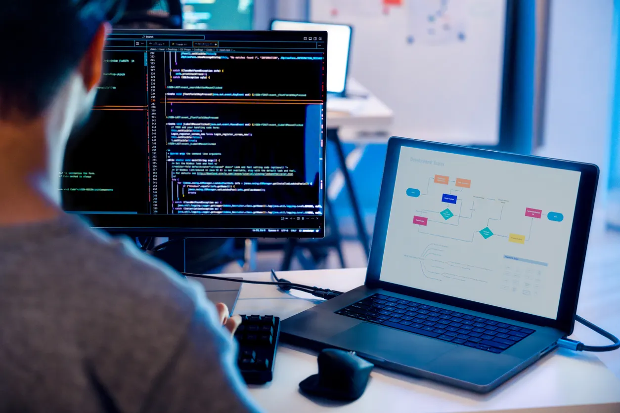 Developer workstation with dual monitors showing website code and a content management dashboard.