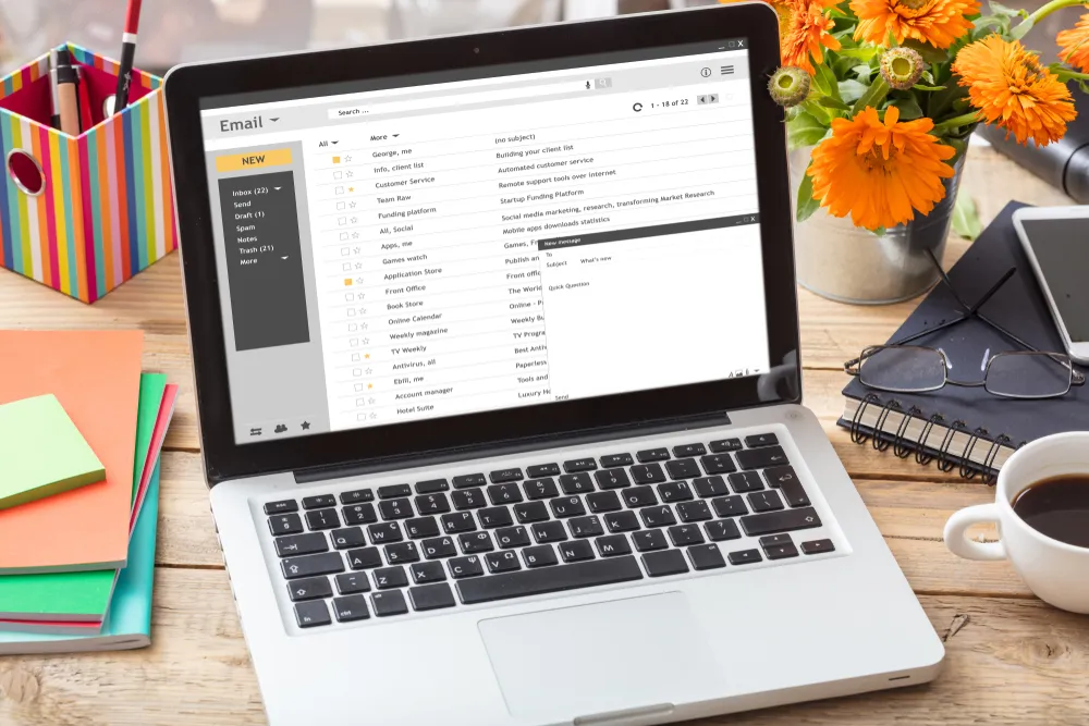 Laptop showing an email inbox on a desk beside a notepad
