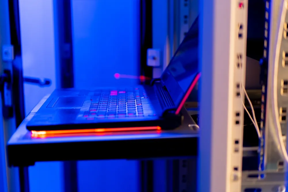 Server rack with patch cables and a laptop open on a shelf