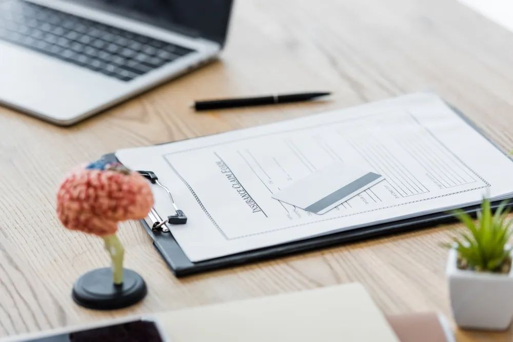 Printed insurance proposal form on a desk beside a laptop and a pen