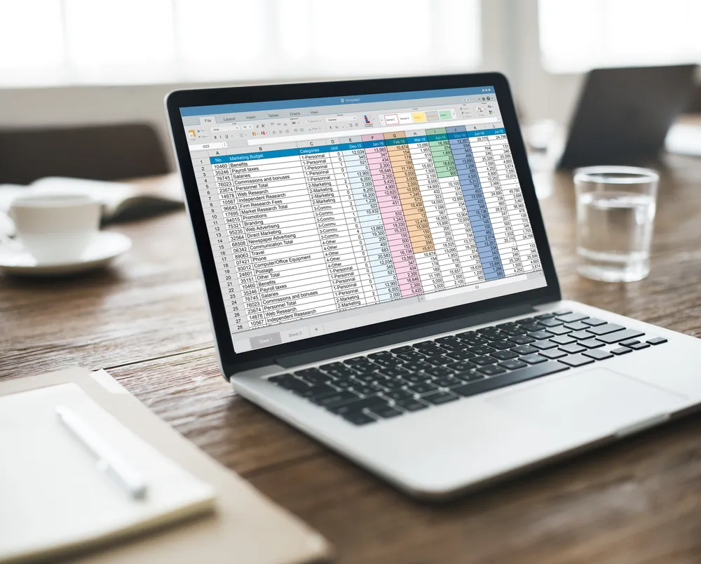 Laptop displaying a spreadsheet on an office desk next to a notepad.