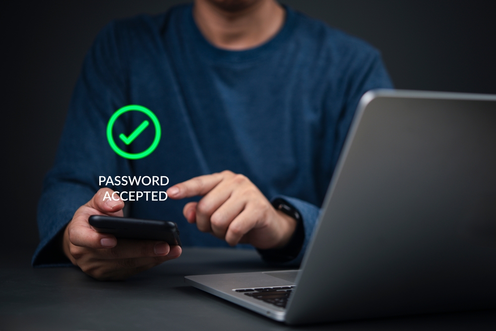 Staff member approving a sign-in prompt on a mobile phone beside a laptop.