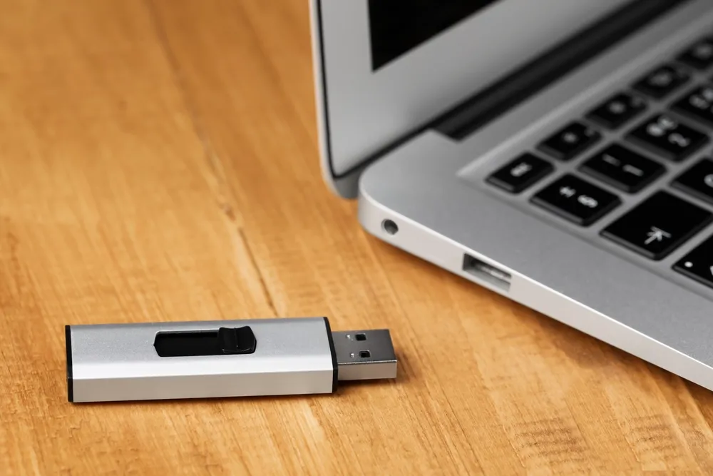 Laptop on an office desk with a USB flash drive beside it.