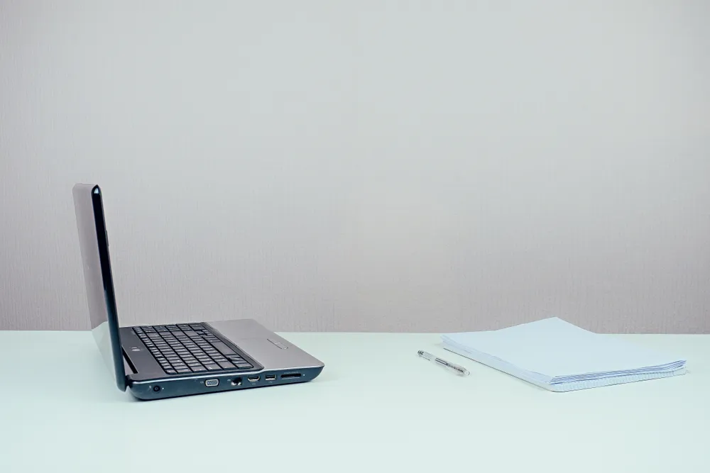 Printed policy document and pen beside a laptop on a desk.