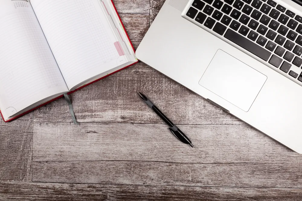 Laptop open on an office desk beside a notepad.