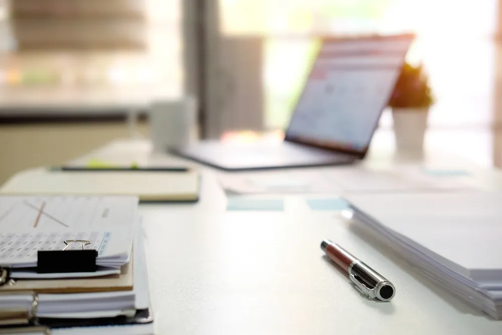 Printed policy document and pen on an office desk beside a laptop.