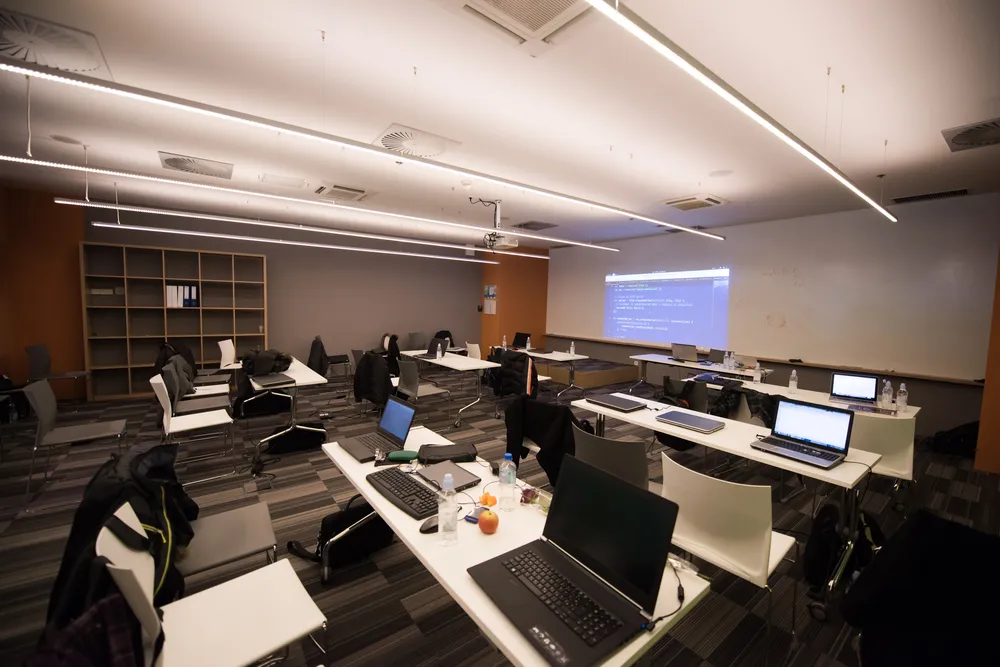 Empty classroom with student laptops on desks and a wall mounted display